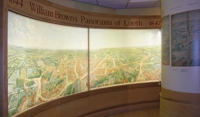 A panorama display of a birdseye map in a museum room, which wraps around a two walls.