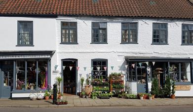 The exrerior of a florist ith many plants outside the doorway.