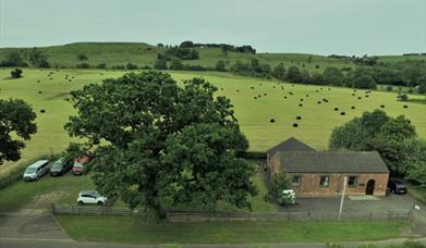 A birdseye view of a hostel surrounded by a field and hills  in the distance.