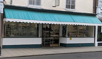 The outside of a butchers shop on the street with large glass windows displaying meats and pies.